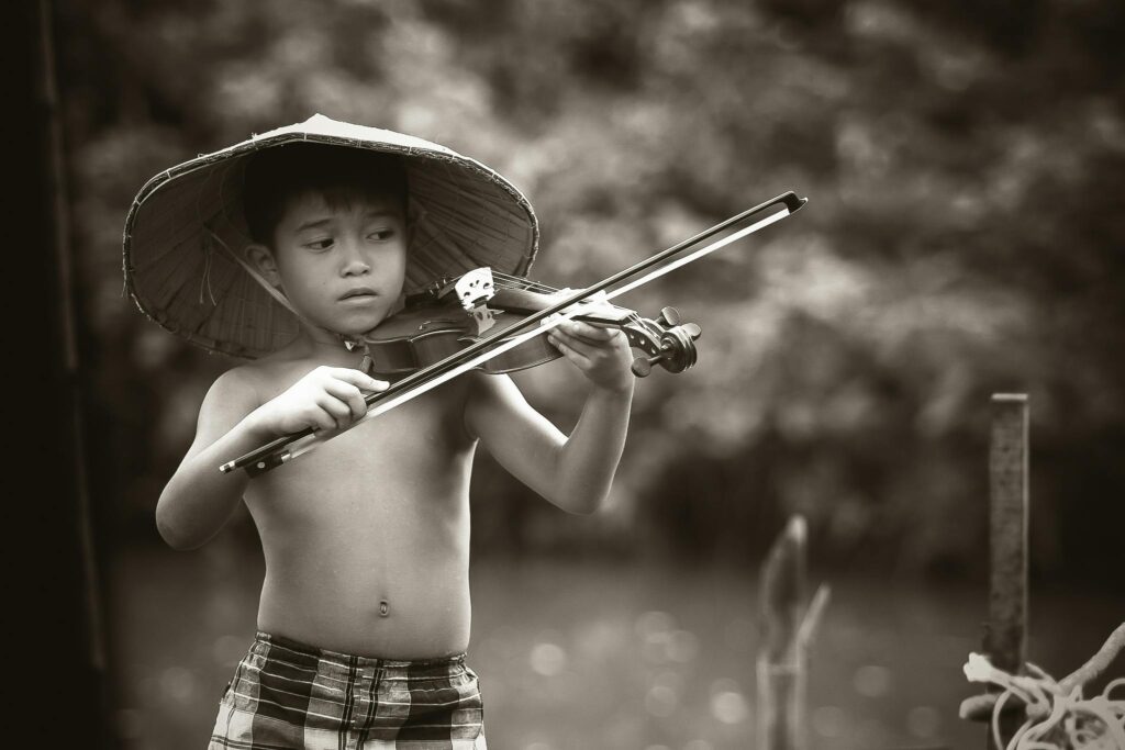 A young boy with a traditional hat plays the violin outdoors, showcasing musical talent and passion.