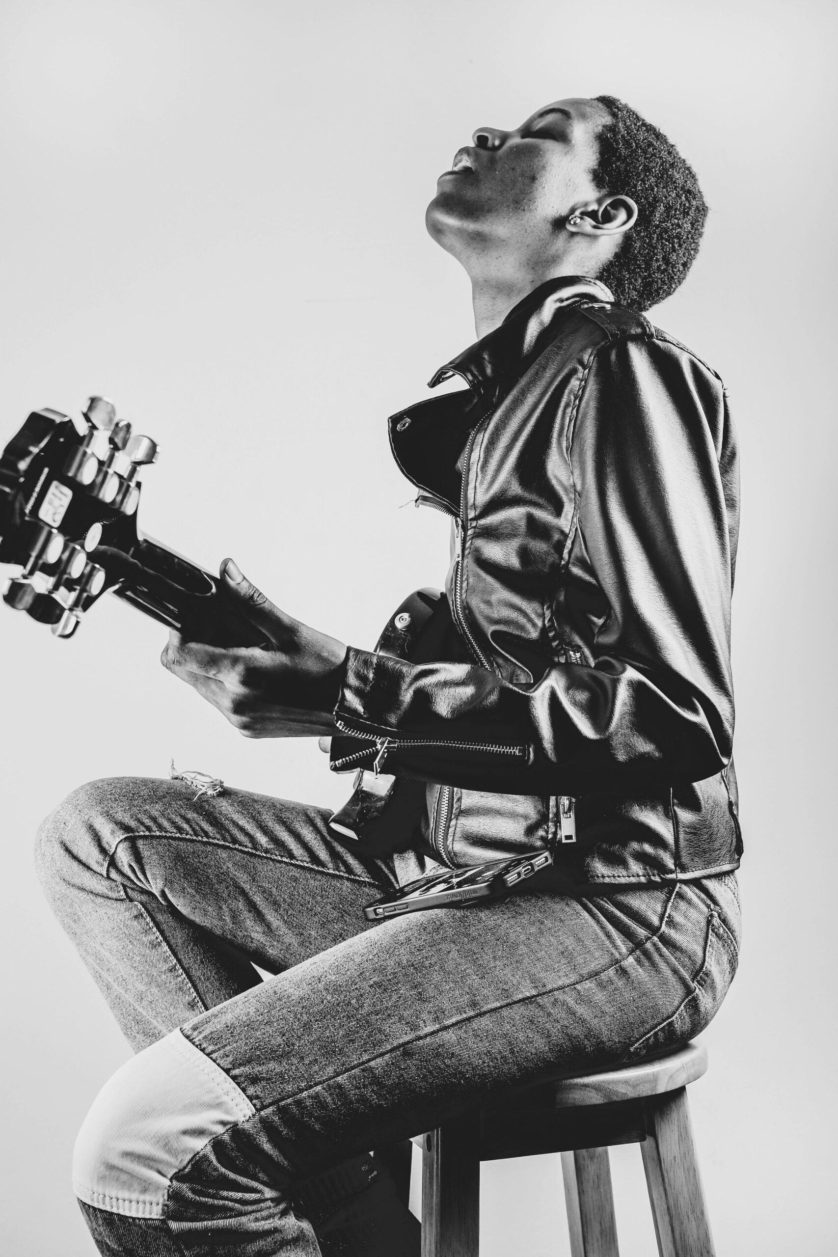 Artistic black and white portrait of a person playing guitar, wearing a leather jacket and jeans.